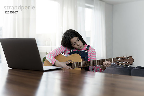 Mädchen spielt Gitarre vor dem Laptop