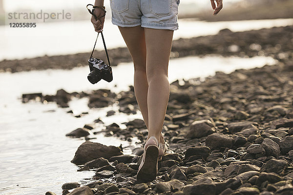 Frau hält eine Kamera in der Hand  die am steinigen Strand läuft