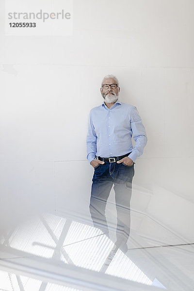 Erwachsener Mann mit Bart und Brille an einer Wand stehend