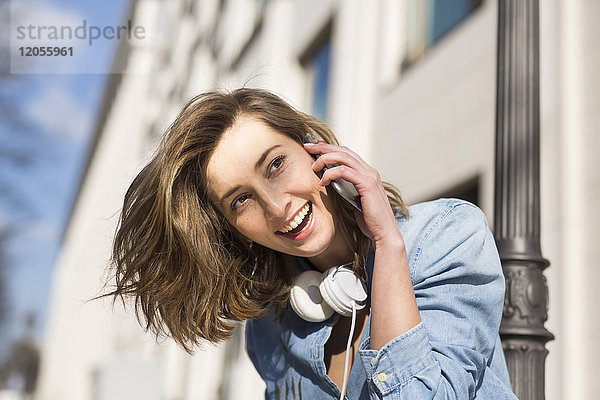 Porträt der lachenden Frau mit Kopfhörer am Telefon