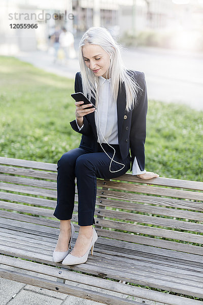 Junge Geschäftsfrau sitzt auf der Bank mit Handy und Kopfhörer
