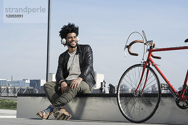 Lächelnder Mann  der Musik über Kopfhörer neben seinem Fahrrad hört.