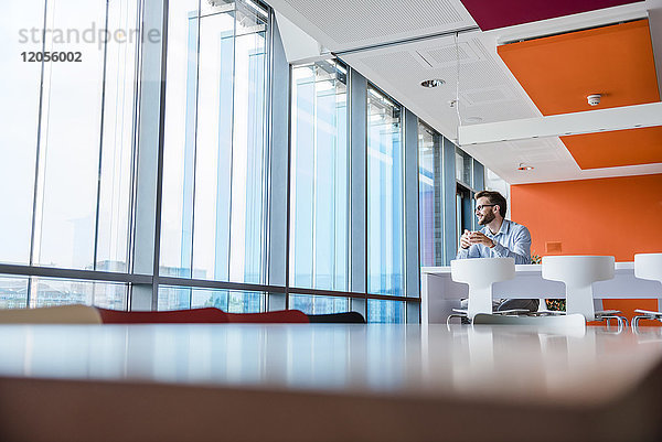 Mann mit Kaffeetasse sitzend in einem modernen Bürogebäude