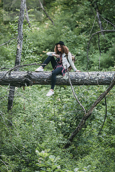 Teenagermädchen mit Kamera auf Totholz in der Natur sitzend