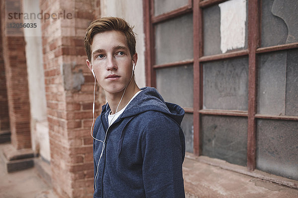 Junger Mann mit Kopfhörern im Backsteingebäude schaut sich um