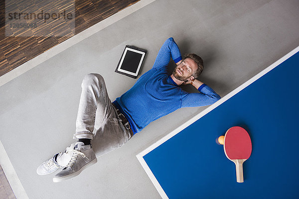 Mann auf dem Boden liegend mit Tablette im Pausenraum des modernen Büros