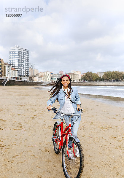 Spanien  Gijon  junge Frau beim Radfahren am Strand