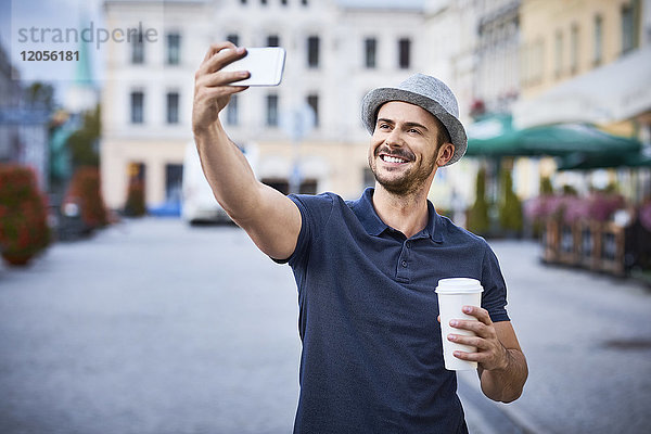 Mann  der Selfie in der Stadt mit Kaffee und Filzhut nimmt
