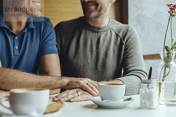 Homosexuelles Paar  das seine Hände mit Eheringen im Cafe zusammensetzt