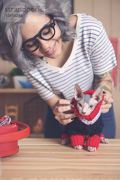 Frau  die zu Hause einen Pullover auf ihre Sphynx-Katze zieht.