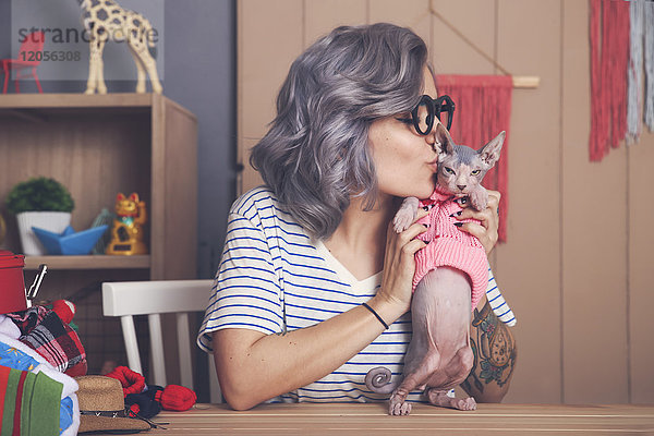 Junge Frau hält und küsst Sphynx-Katze mit Pullover