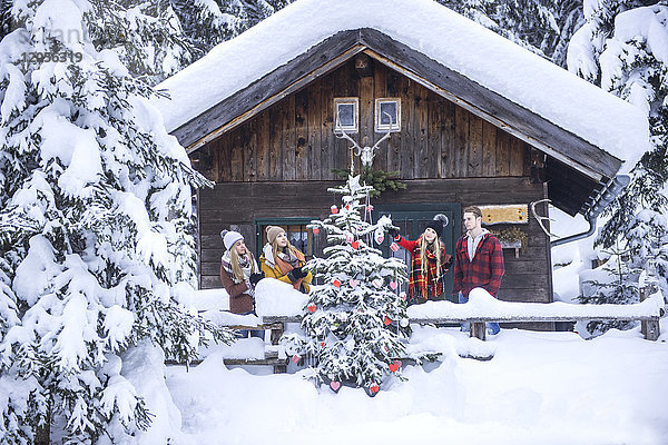 Österreich  Altenmarkt-Zauchensee  Freunde schmücken Weihnachtsbaum im Holzhaus
