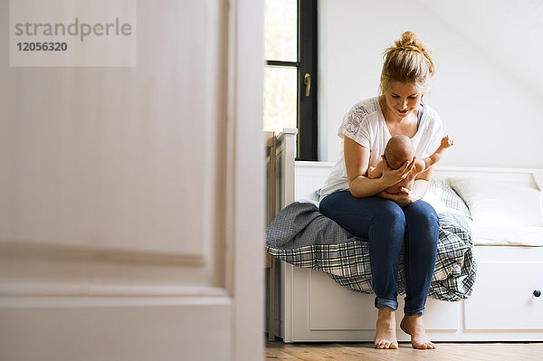 Mutter sitzt auf dem Bett und hält das kleine Baby.