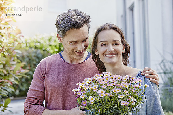 Porträt eines lächelnden Paares mit Blumen vor dem Haus