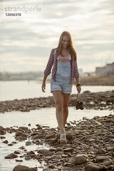 Junge Frau mit Kamera am steinigen Strand