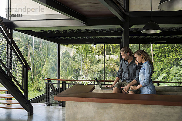 Lächelndes Paar mit Laptop in moderner minimalistischer Küche im zeitgenössischen Designhaus