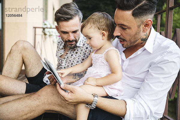 Schwules Paar mit Tochter auf dem Balkon mit digitalem Tablett
