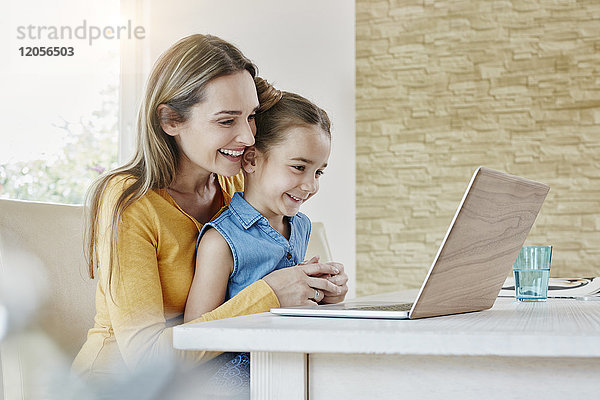 Glückliche Mutter mit Tochter zu Hause auf dem Laptop