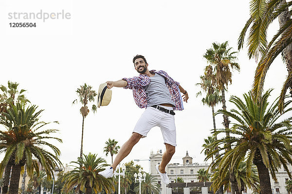 Spanien  Barcelona  glücklicher Mann  der in der Luft springt  umgeben von Palmen.