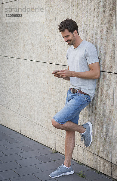 Mann lehnt sich an die Wand  mit dem Smartphone