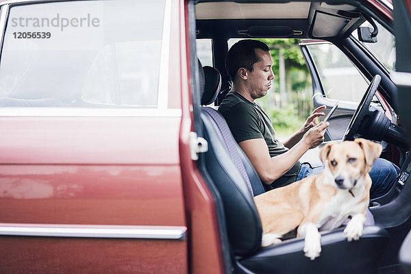 Mann mit Tablette im Auto mit Hund auf Beifahrersitz