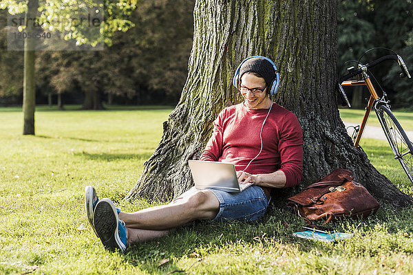 Mann mit Laptop und Kopfhörer im Park