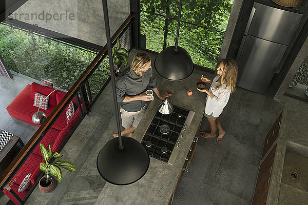 Draufsicht auf das Paar in einer modernen Designküche mit Glasfassade  umgeben von einem üppigen Garten.