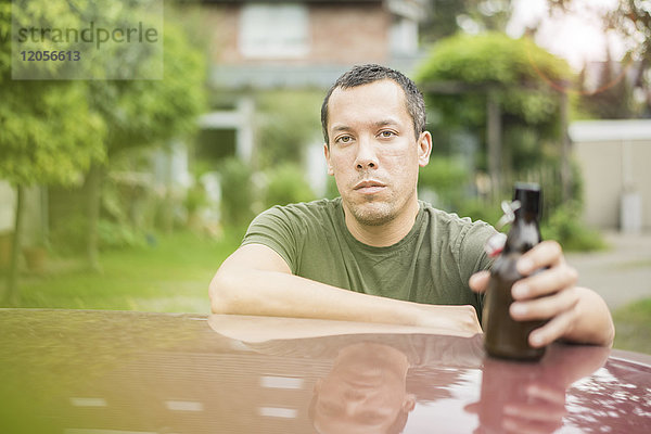 Porträt eines seriösen Mannes mit Bierflasche auf dem Autodach