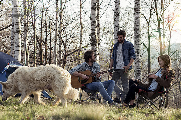 Freunde campen im Wald mit einem Mann  der Gitarre spielt.