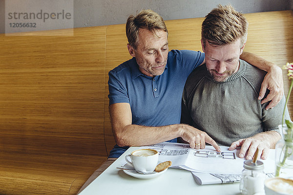 Homosexuelles Paar  das sich Baupläne für sein Haus im Café ansieht.