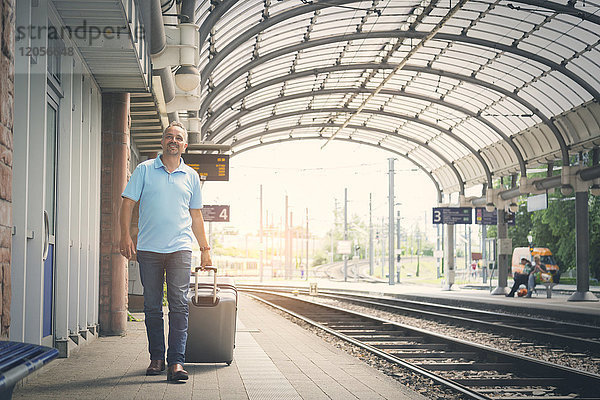 Lächelnder Mann mit Gepäck auf dem Bahnsteig