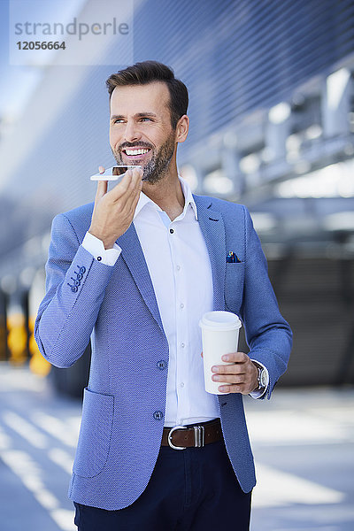 Porträt des lächelnden Geschäftsmannes mit Telefon und Kaffee in der Stadt