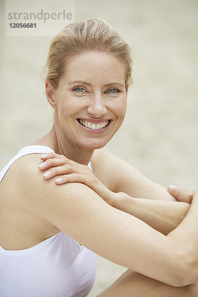 Porträt einer lachenden  blonden Frau  die am Strand sitzt