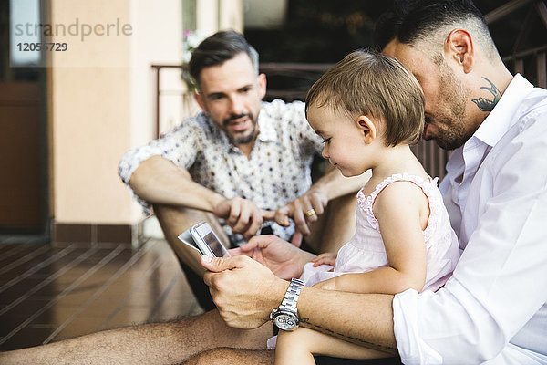 Schwules Paar mit Tochter auf dem Balkon mit digitalem Tablett