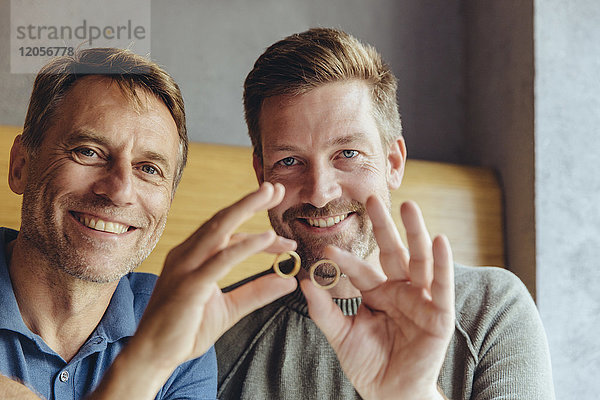 Glückliches schwules Paar  das seine Eheringe hochhält.