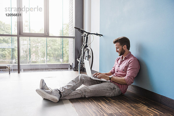 Mann mit Laptop im Büro auf dem Boden sitzend