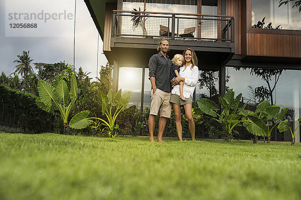 Porträt einer lächelnden Familie  die vor ihrem Designhaus steht  umgeben von einem üppigen tropischen Garten.