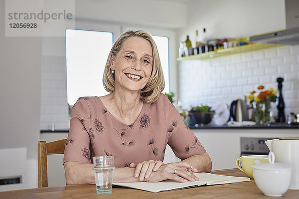 Porträt der lächelnden reifen Frau mit Notizbuch am Küchentisch