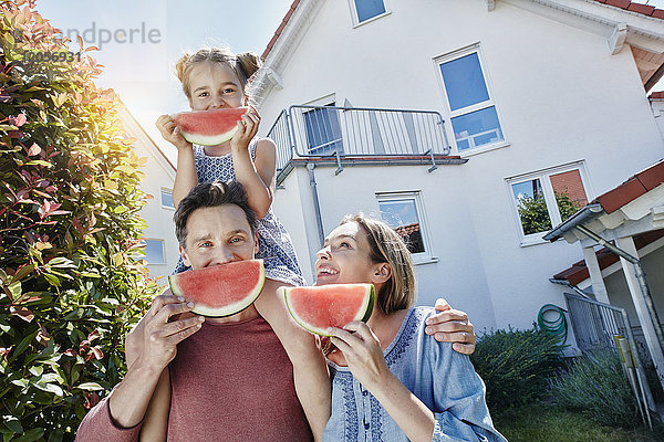 Porträt einer glücklichen Familie mit Wassermelonenscheiben vor dem Haus