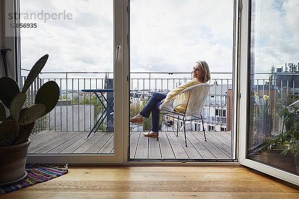 Lächelnde reife Frau zu Hause auf dem Balkon sitzend