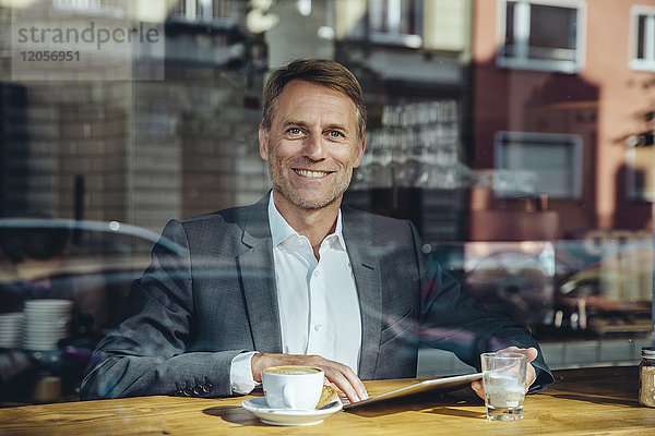 Porträt eines lächelnden Geschäftsmannes mit Tablette im Café