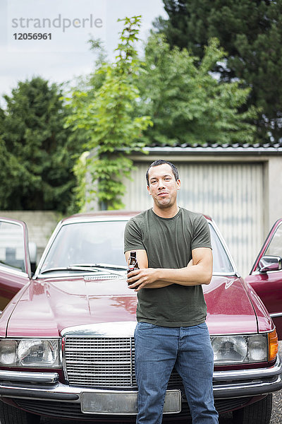 Porträt eines selbstbewussten Mannes mit Bierflasche vor dem Auto stehend