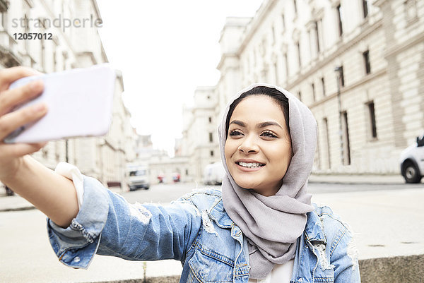 UK  England  London  junge Frau mit Hijab  die einen Selfie in der Stadt macht.