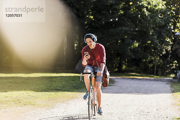 Mann auf Rennrad mit Blick auf Handy im Park