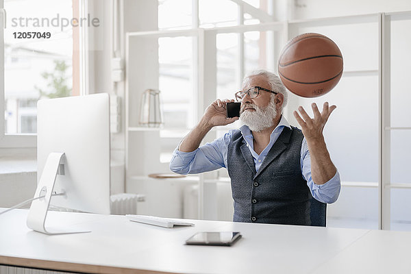 Erwachsener Mann auf dem Handy am Schreibtisch beim Basketballspielen