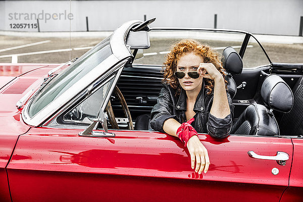 Porträt einer rothaarigen Frau mit Sonnenbrille im Sportwagen
