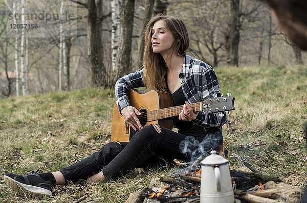 Frau spielt Gitarre im Wald am Lagerfeuer