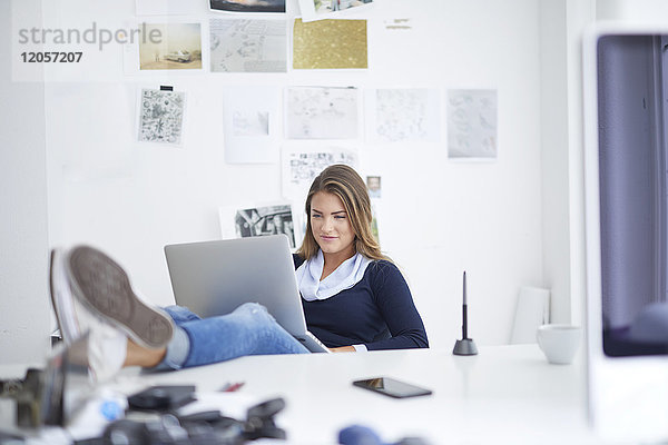 Lächelnde junge Frau mit Laptop am Schreibtisch im Büro