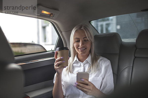 Lächelnde Geschäftsfrau mit Kaffee zum Mitnehmen und Handy im Auto