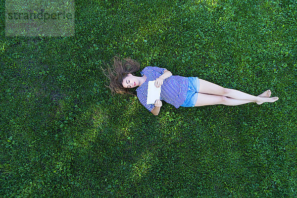 Junge Frau auf Gras liegend  mit digitaler Tafel